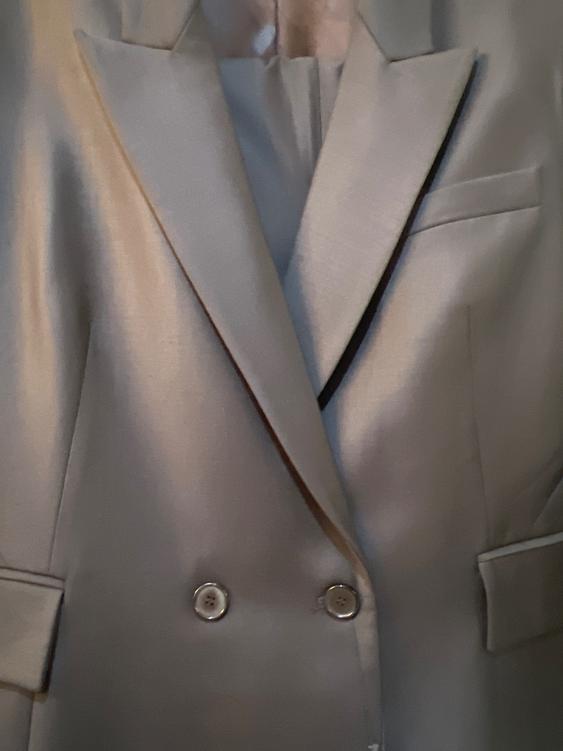 Close-up of a gray blazer with wide lapels and double-breasted closure. Shiny fabric and flap pockets.