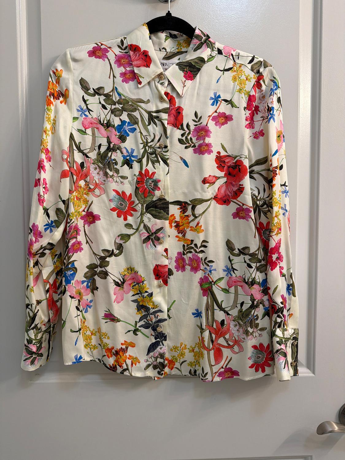 Multicolor floral print long-sleeve shirt on a white background, hanging on a black hanger in front of a white door.