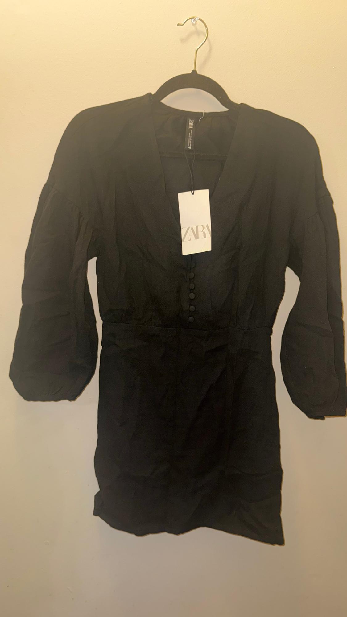 Long-sleeved black dress hanging on a hanger, with a visible Zara tag. Beige background.