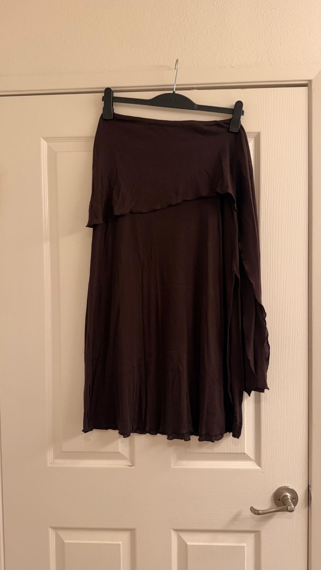 Brown skirt hanging on a black hanger over a white door. The skirt has an asymmetrical, flowing design.
