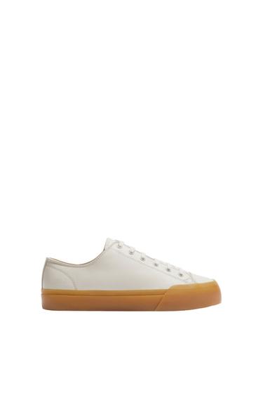 Low-profile white trainer with a light brown rubber sole, side view on a white background. Minimalist and modern design.
