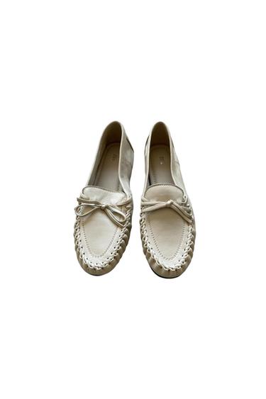 Light beige loafers with braided stitching and a bow on the front, set against a white background. Interior text: ZARA.