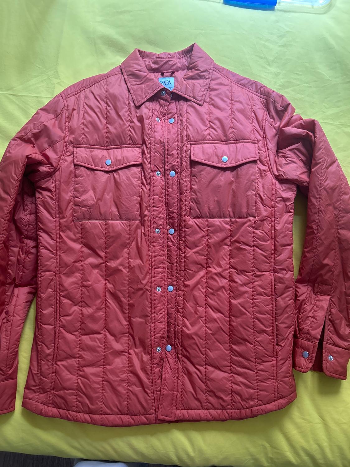 Red padded shirt with popper fastenings and chest pockets, on a yellow background. Visible label on the collar.