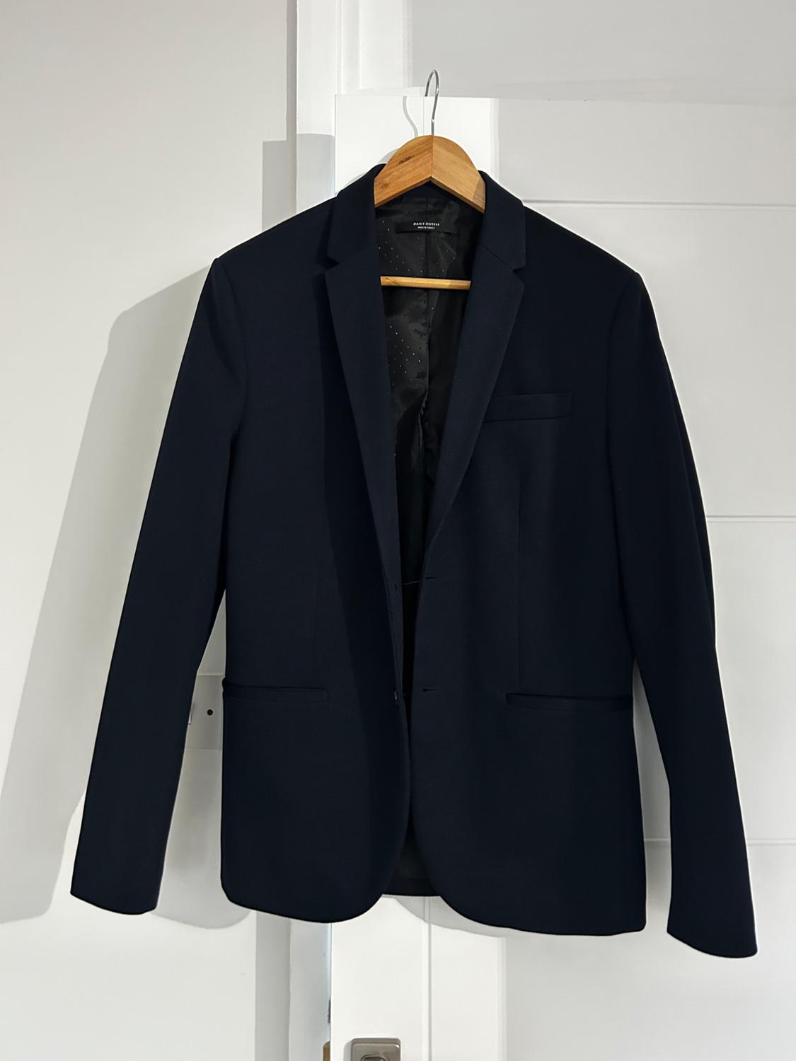 Black jacket hanging on a wooden coat hanger over a white door. Interior with dark lining and subtle detailing.
