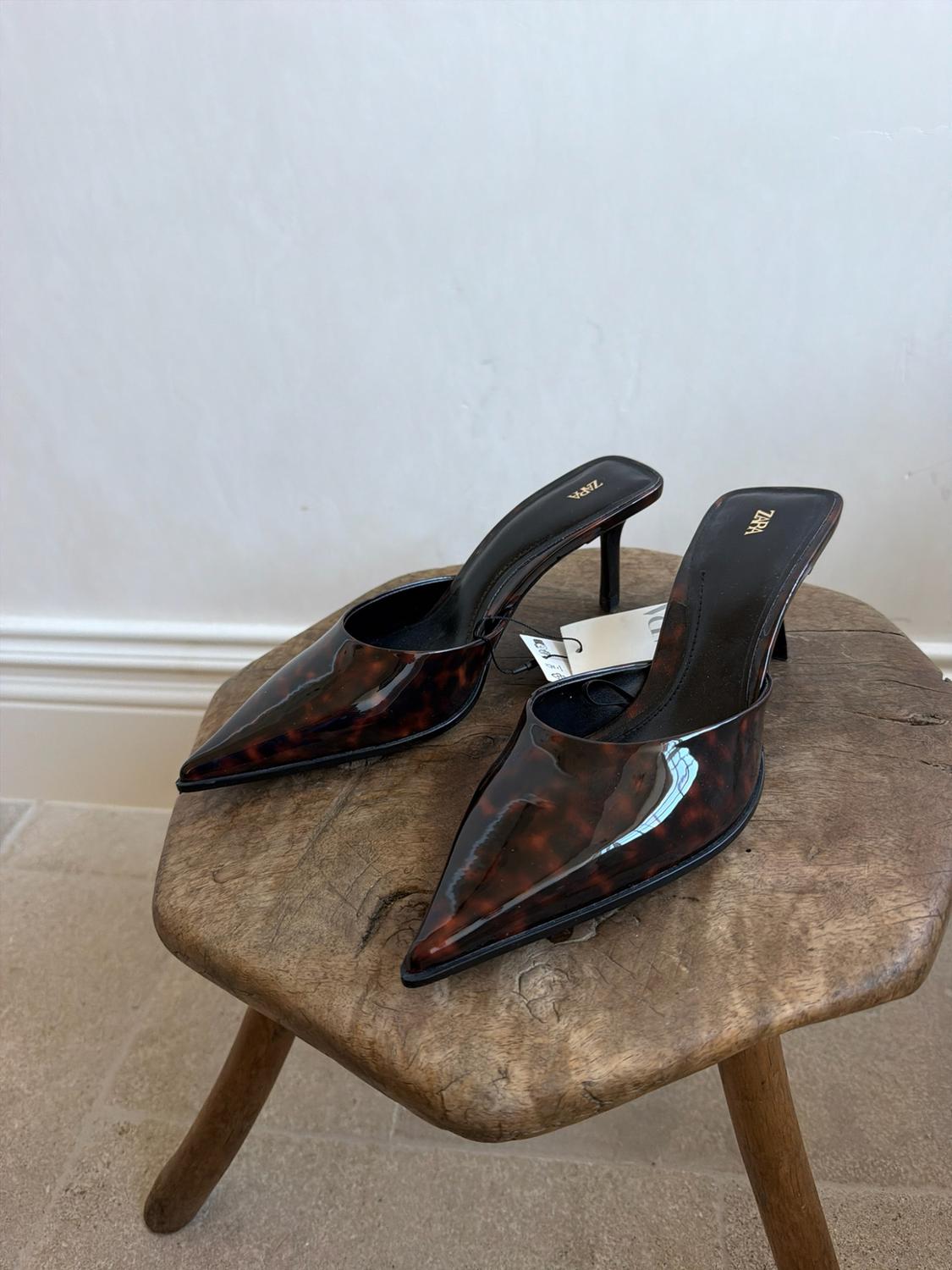 Pointed-toe slingback heels with a glossy tortoiseshell finish on a wooden stool. ZARA text on the insole.