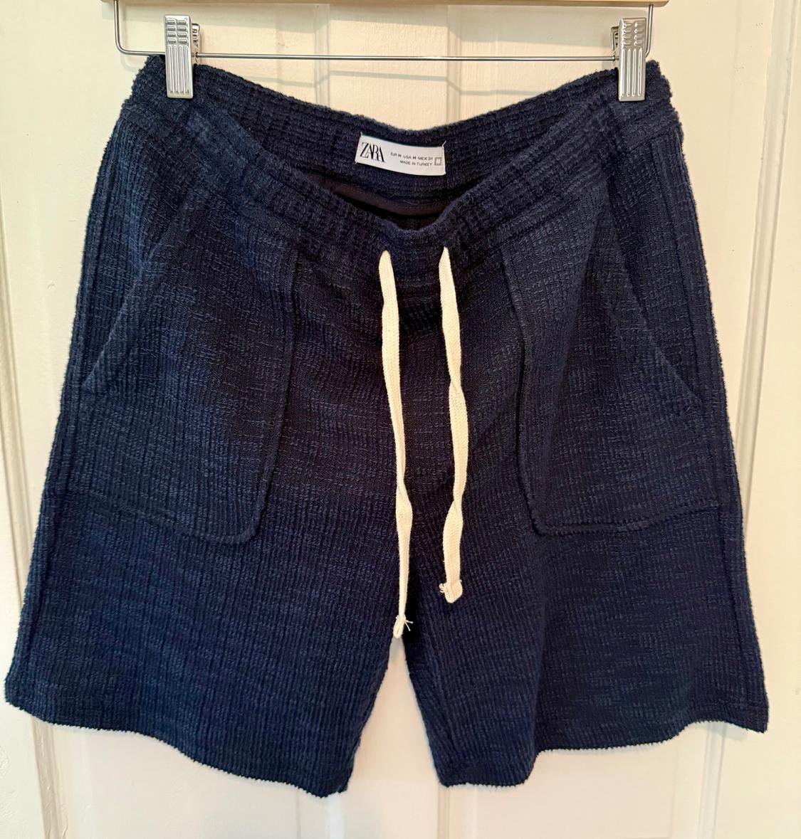 Textured navy blue shorts with white drawstrings and front pockets, hanging on a hanger against a light background.