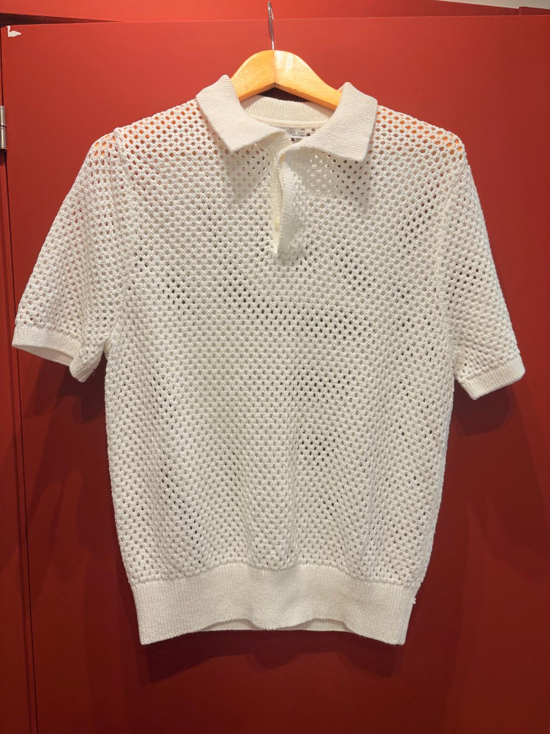 White open-knit polo shirt hanging on a wooden hanger against a red background.