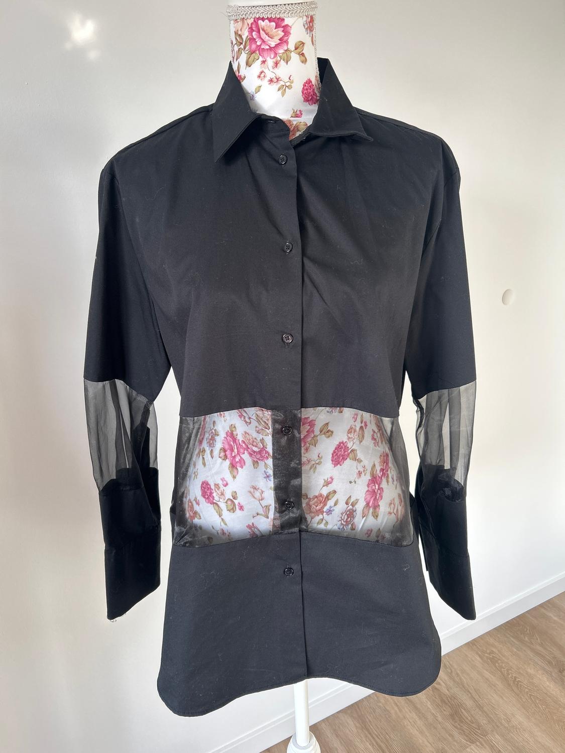Mannequin in a long-sleeved black shirt with sheer panels on the torso and sleeves. White background and wooden floor.