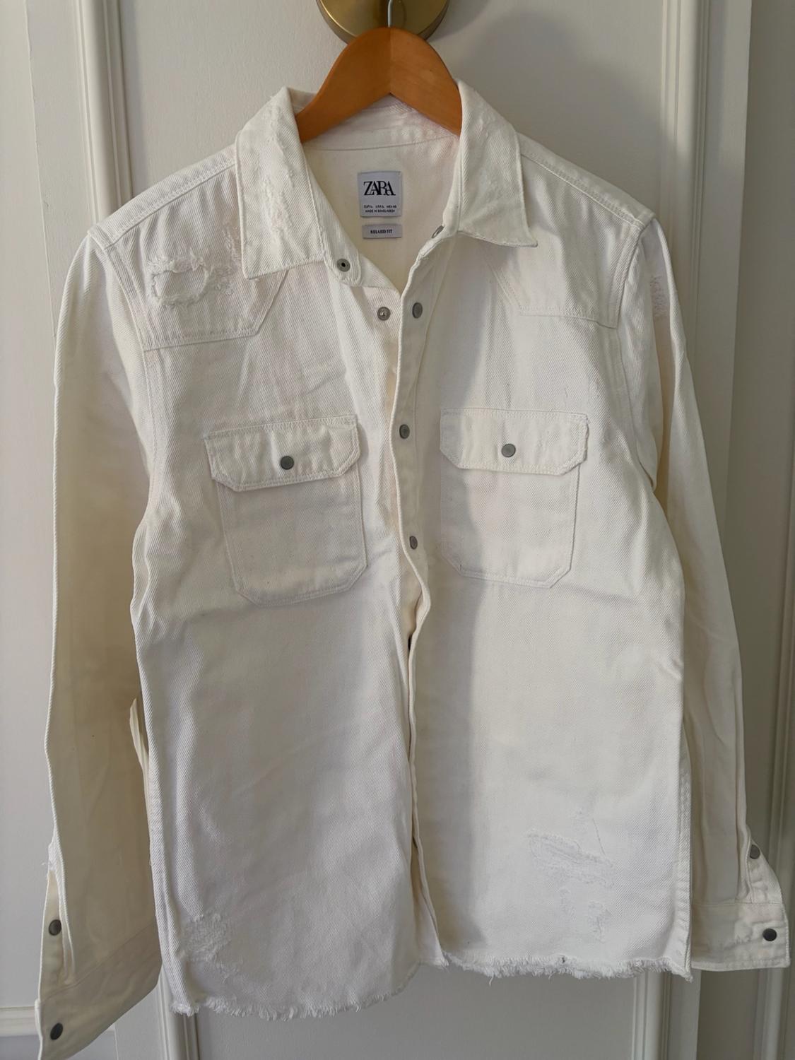 White shirt with pockets, rips and frayed hem on a hanger. Text: ZARA EUR L USA L MEX 42 MADE IN BANGLADESH RELAXED FIT.