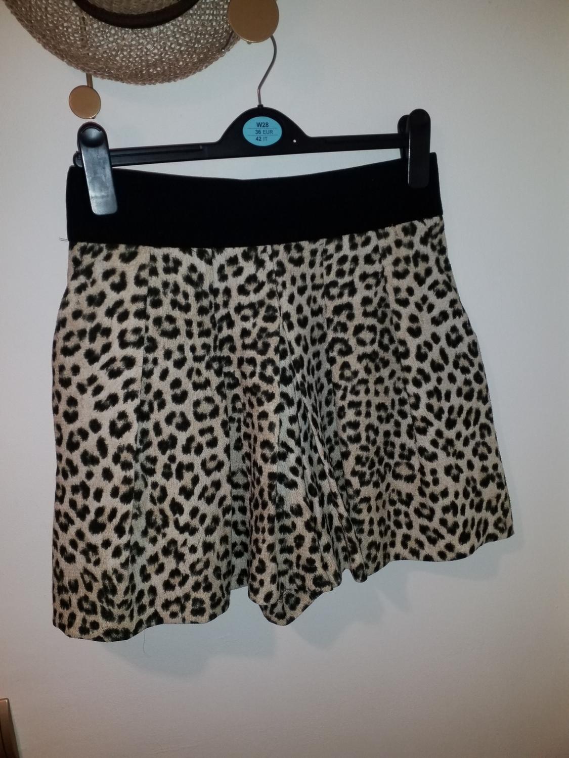 Leopard print skirt on black hanger, white background. Label on hanger: "W28 36 EUR 42 IT". Straw hat hanging above.