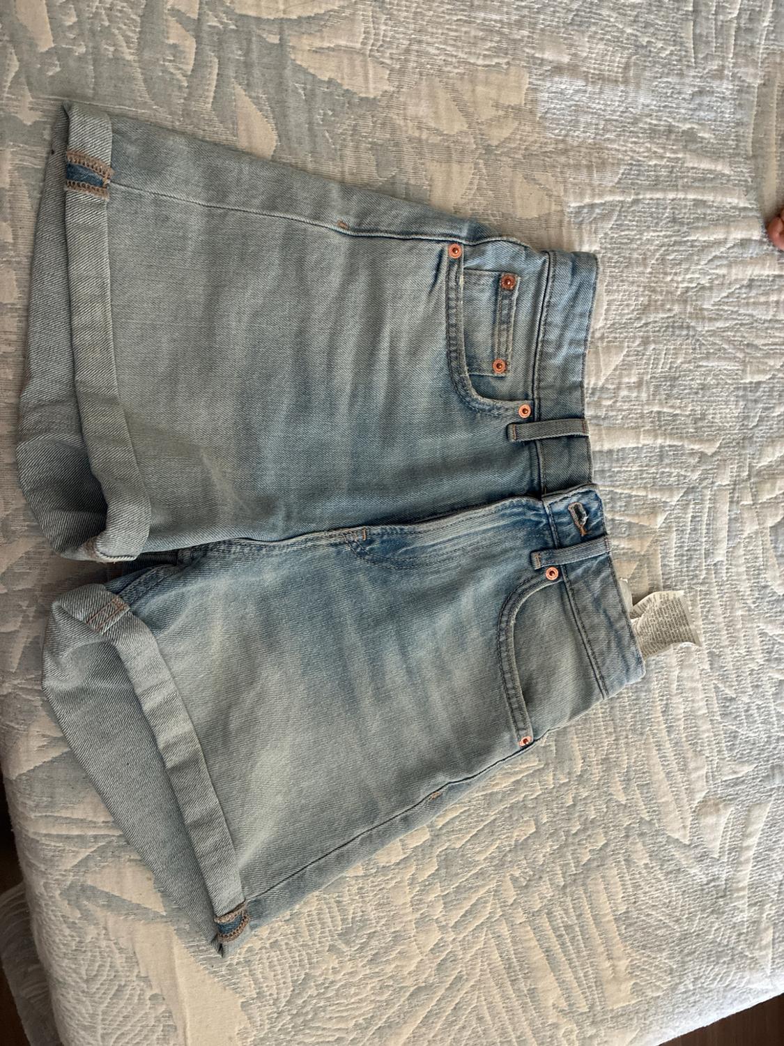 Light blue denim shorts with rolled hems, on a textured bedspread with a white and blue pattern.