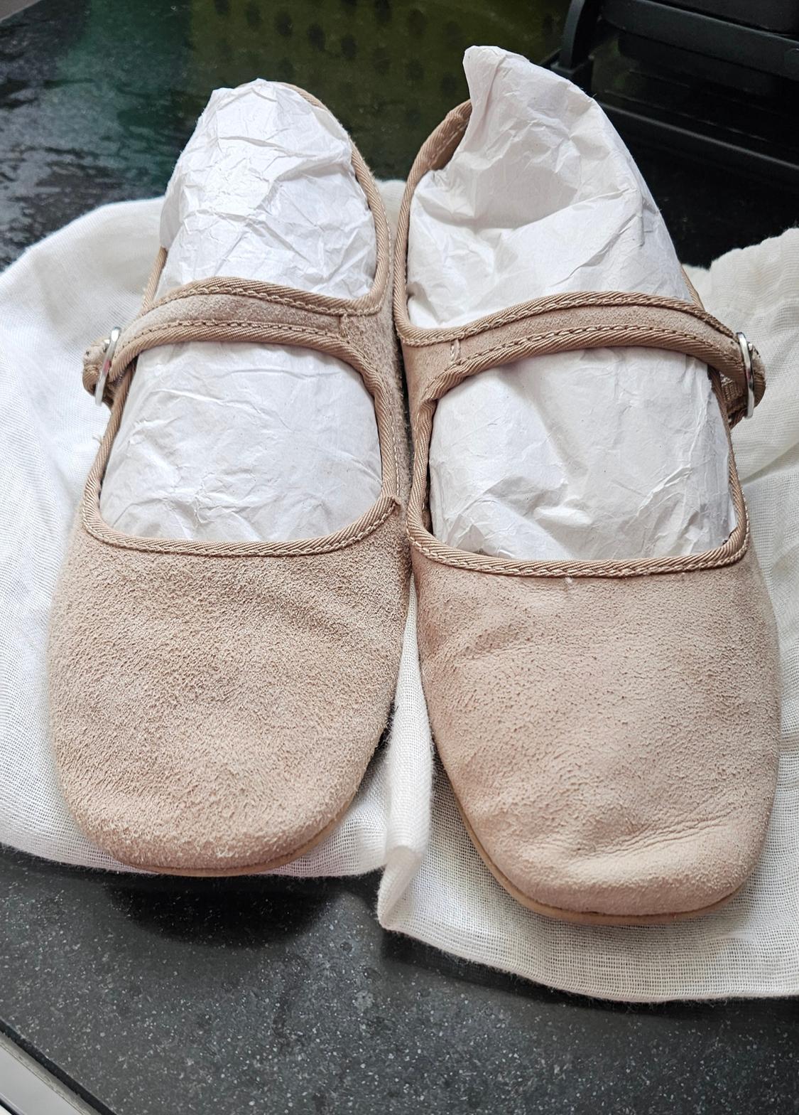 Beige flat shoes with a strap, stuffed with white paper, on white fabric on a dark surface. Casual and comfortable style.