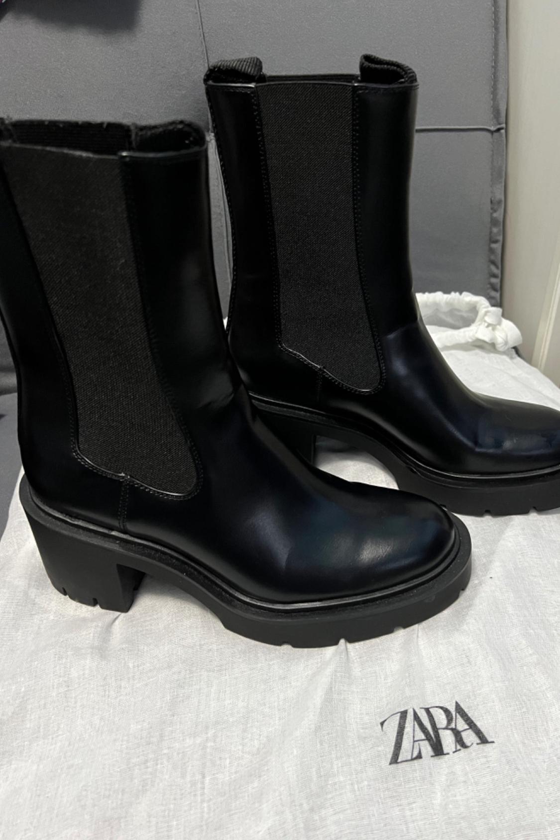 Side view of black boots with elastic side panels and a chunky heel on white fabric with 'ZARA' text.