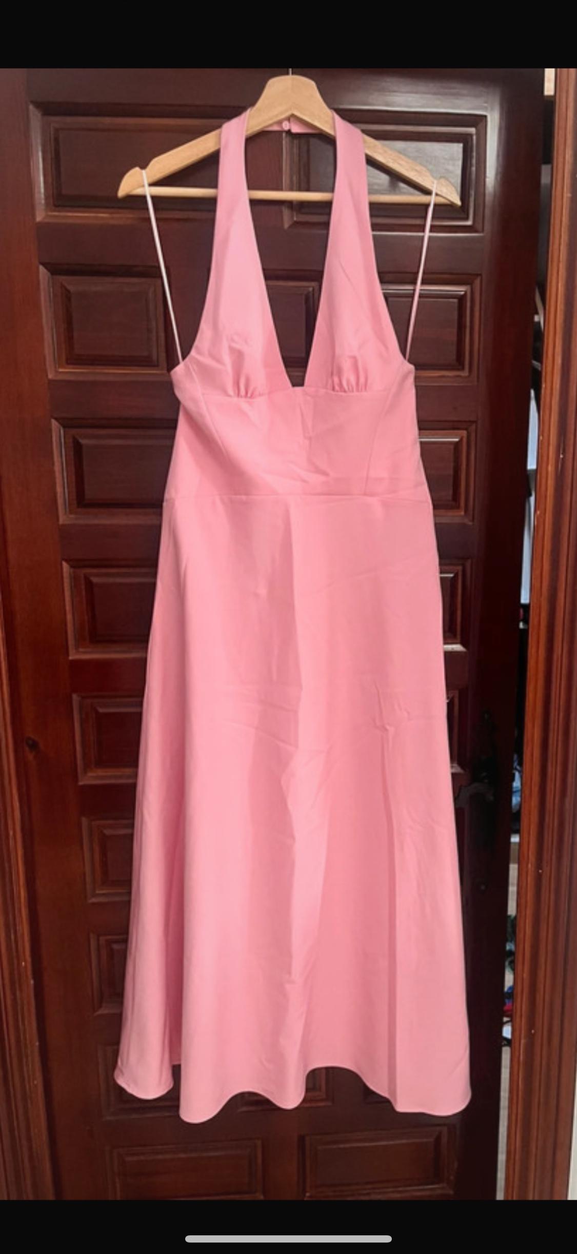 Sleeveless pink dress hanging on a wooden hanger in front of a dark, panelled wooden door.