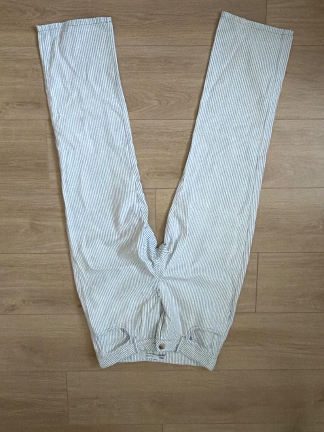 Light pinstriped trousers spread out on a wooden floor. Flat lay composition in a casual style.
