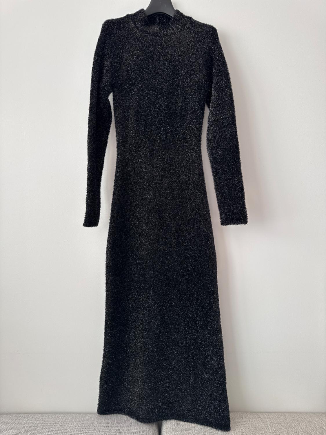 Black long-sleeved, round-neck dress, hanging on a hanger against a white background.