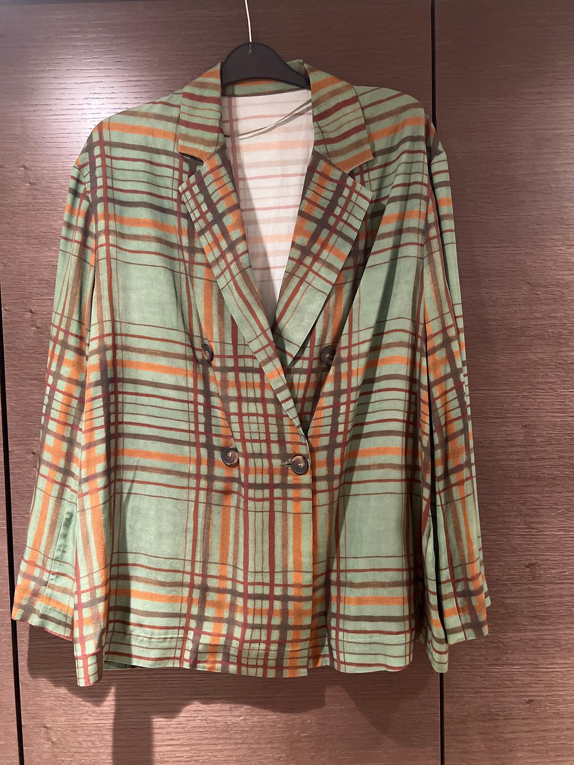 Green and orange plaid jacket hanging on a hanger against a brown wooden background.