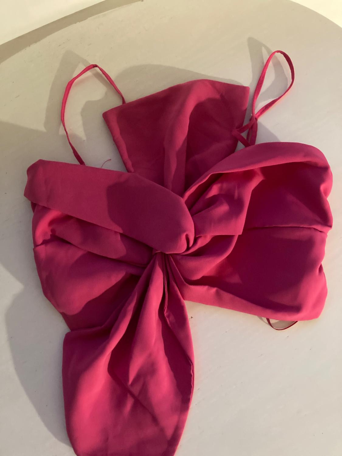 Fuchsia top with thin straps and large bow design, placed on a light surface.