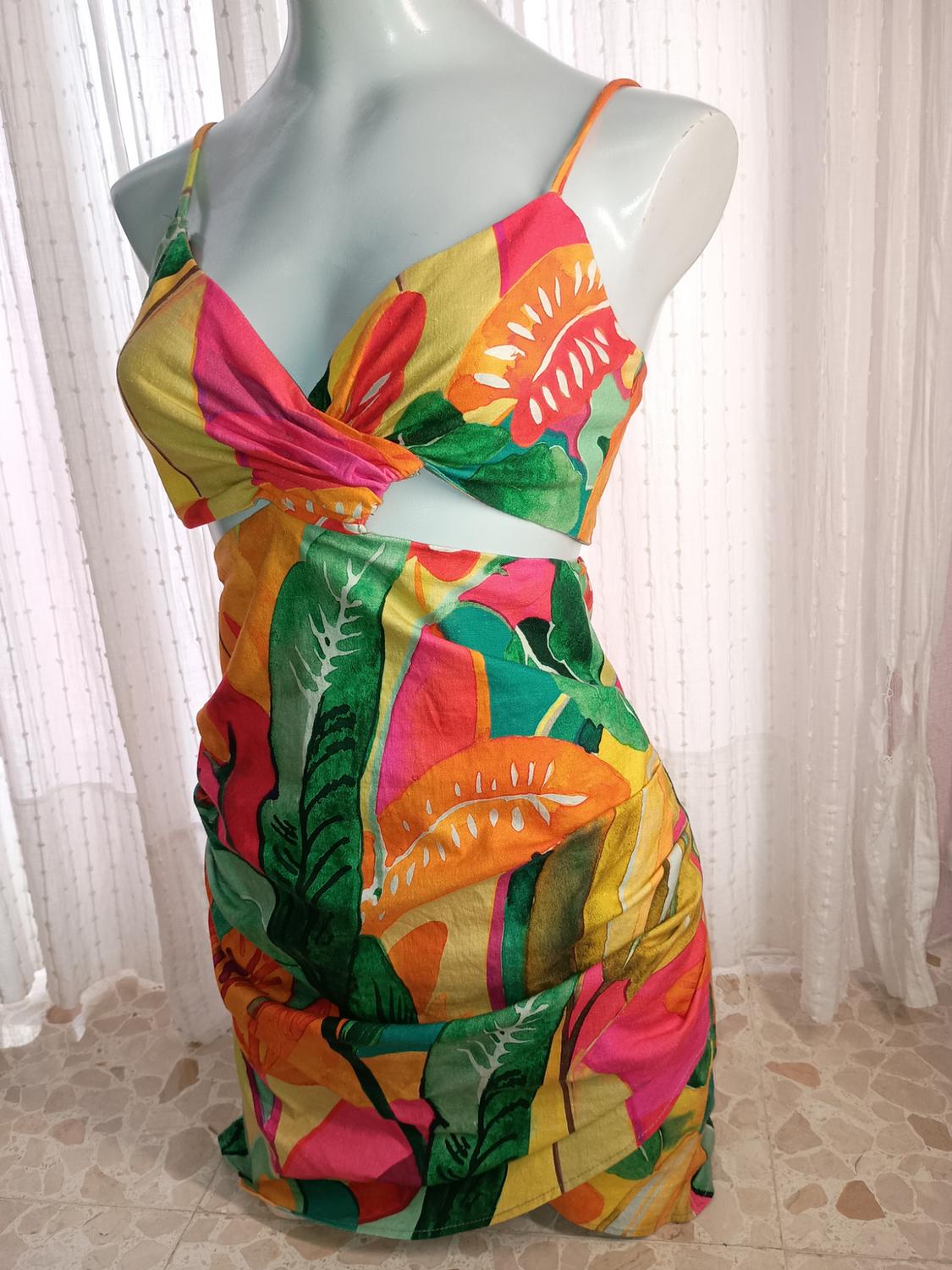 Mannequin in a summery strappy dress, tropical print in vivid colours such as pink, green, and yellow, with a white curtain background.