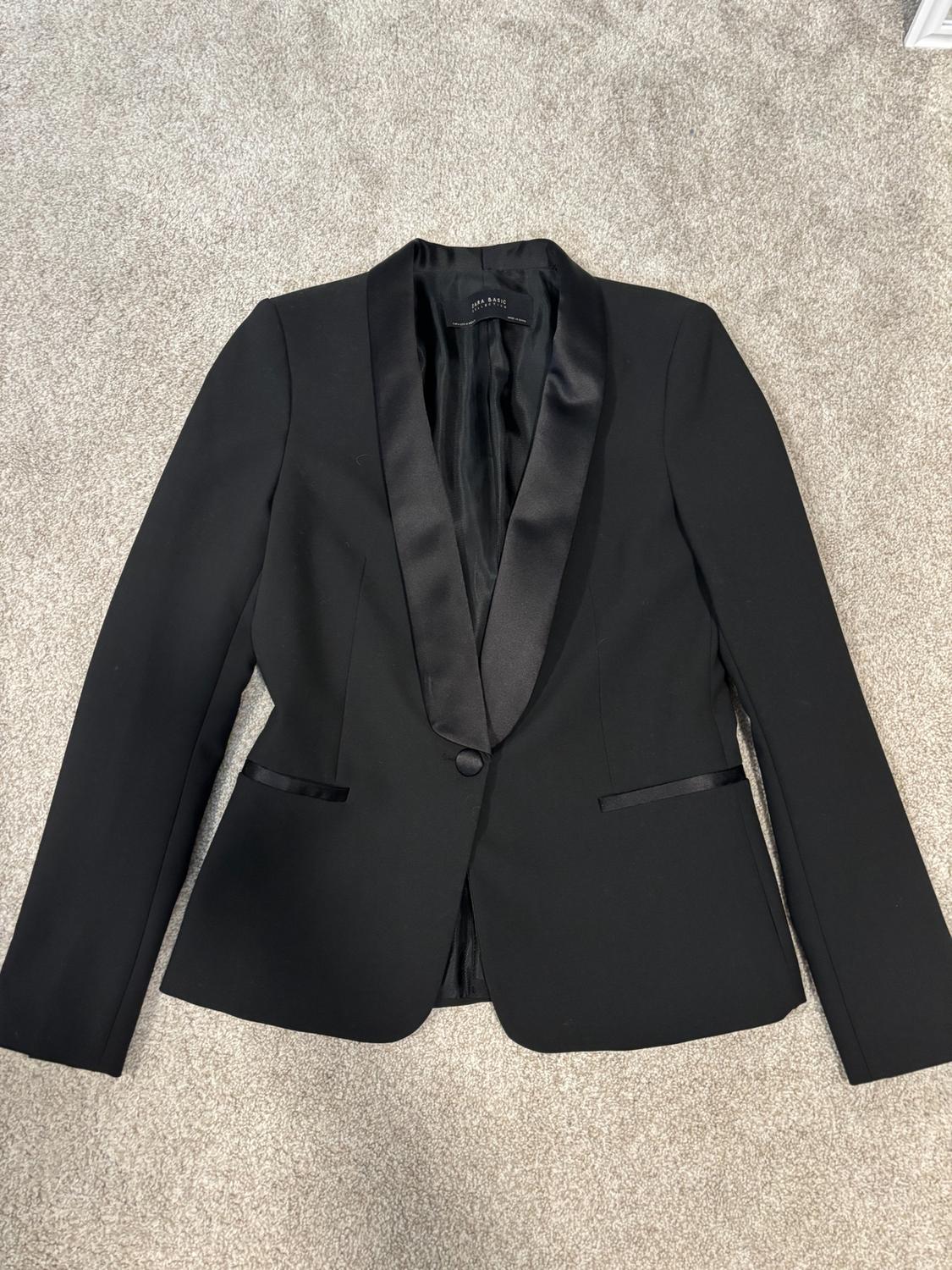 Black satin jacket with lapels and one button, on a gray carpet. Inner label visible at the collar.