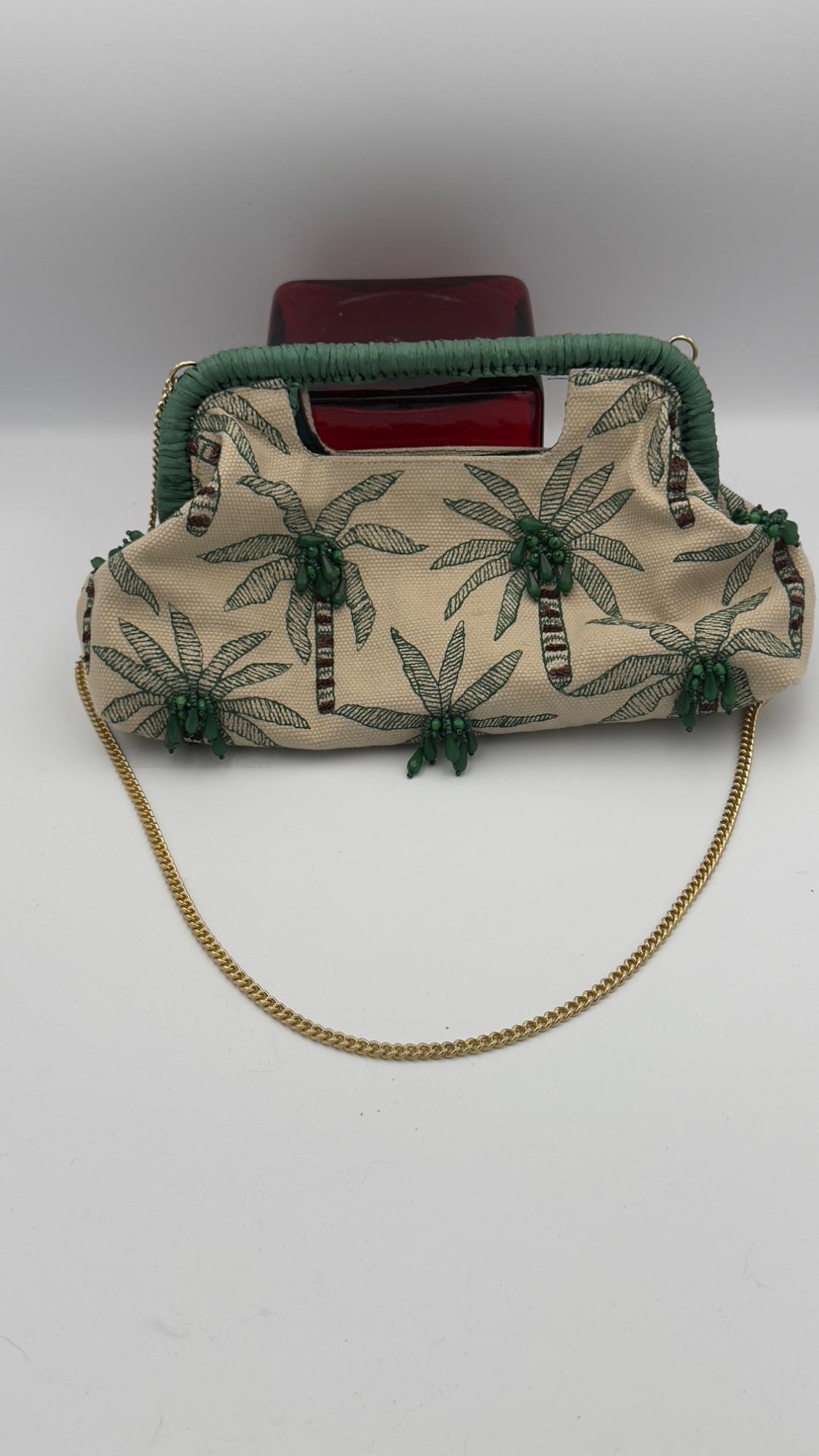 Beige bag with green palm tree print and beaded details, green handle and gold chain on a white background.