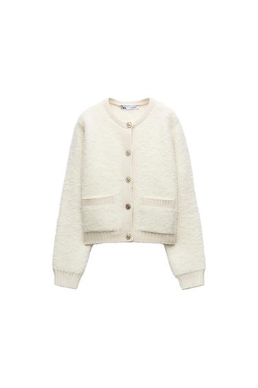 White wool cardigan with buttons and front pockets. Visible label with text "ZARA". White background.