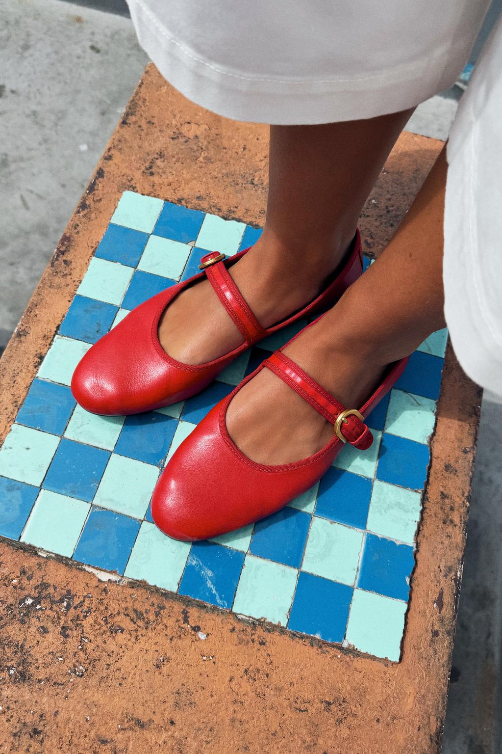 Close-up of red ballet flats with an instep strap, gold buckle closure, and a round toe.