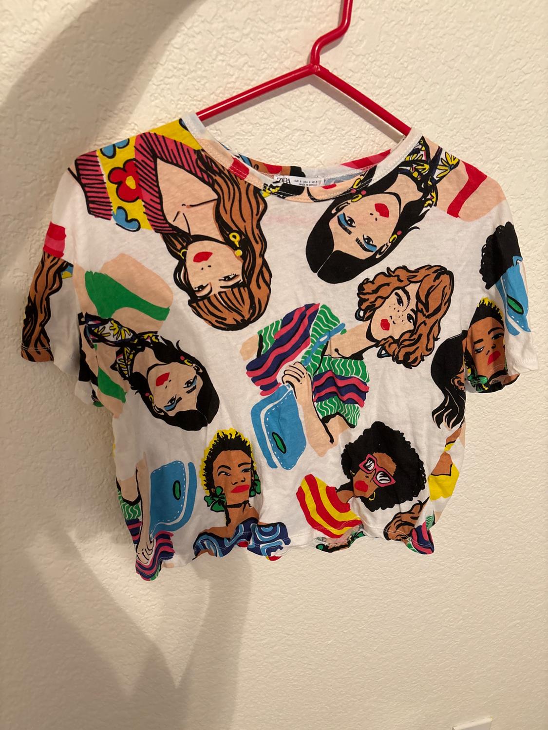 Front view of a t-shirt with a print of women's faces in vibrant colors.