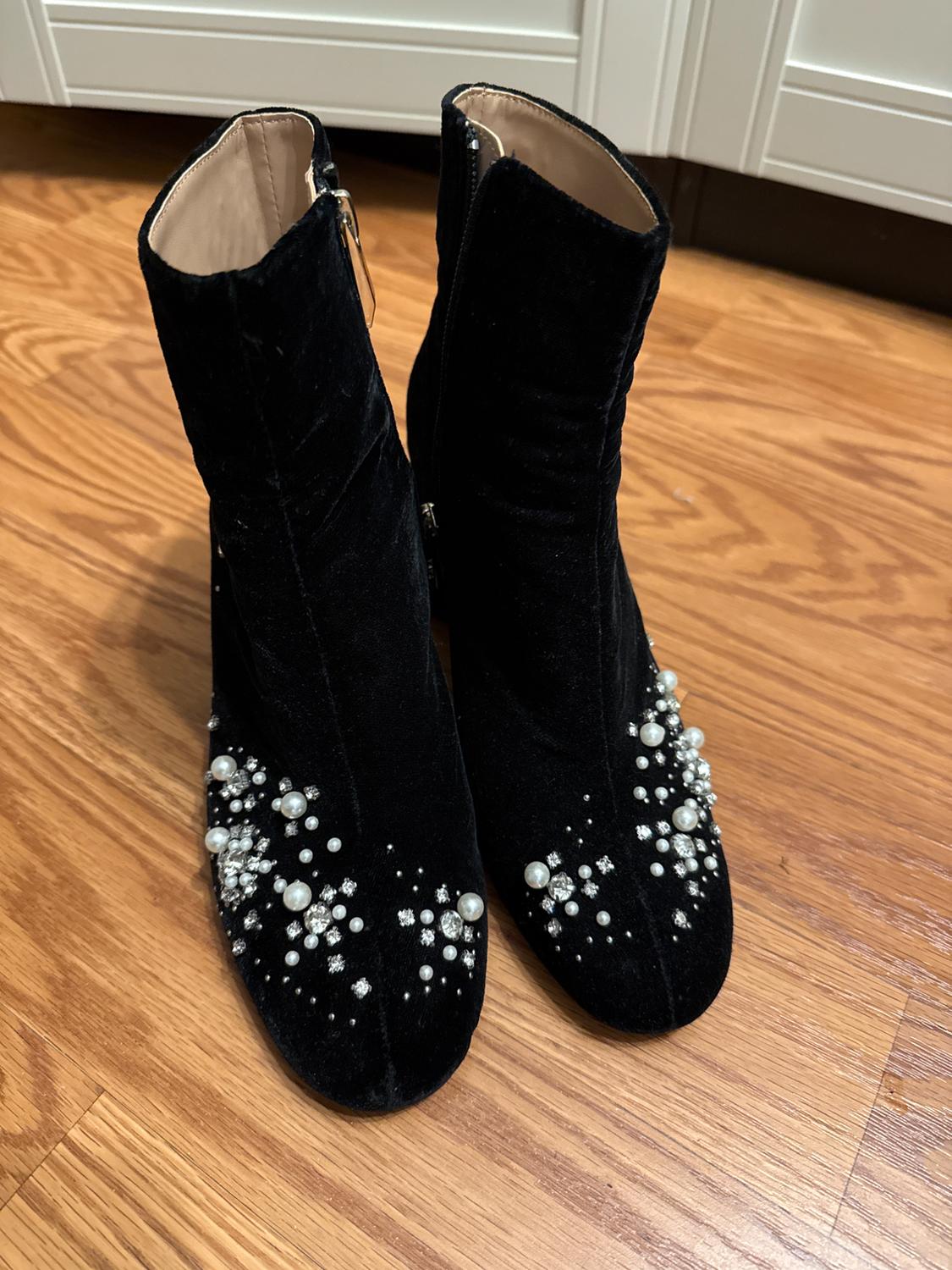 Black velvet boots with decorative pearls and crystals on top, on a light wooden floor.