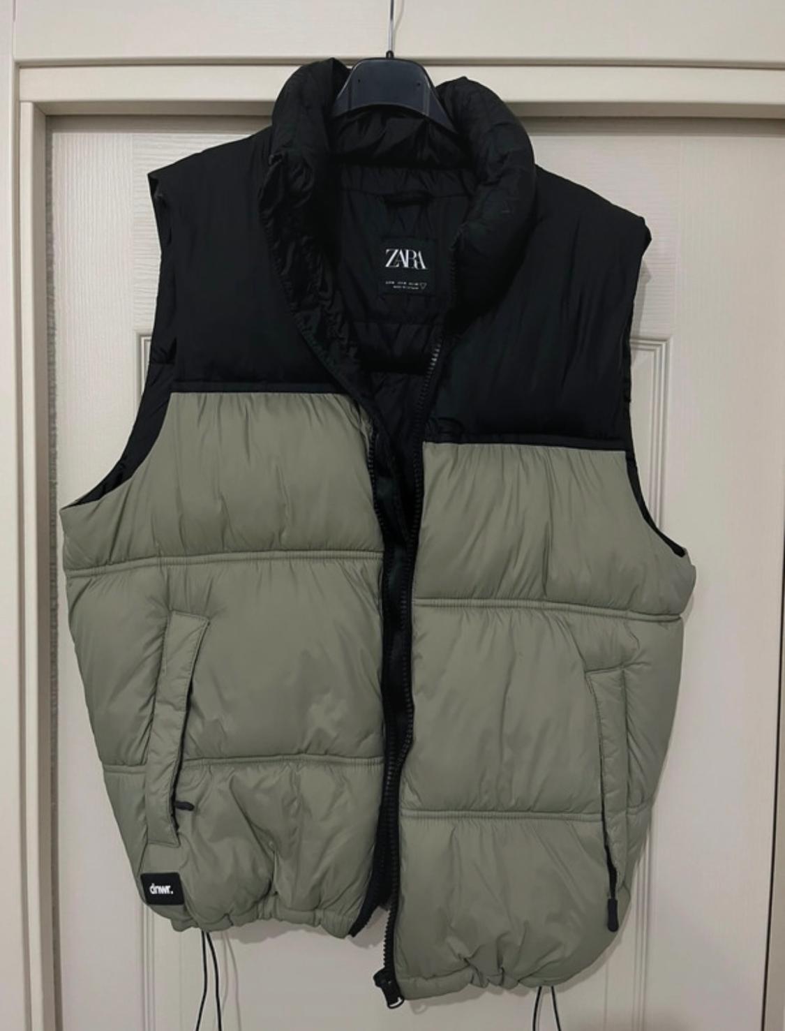 Front view of a black and green two-tone padded gilet with side pockets and zip fastening.