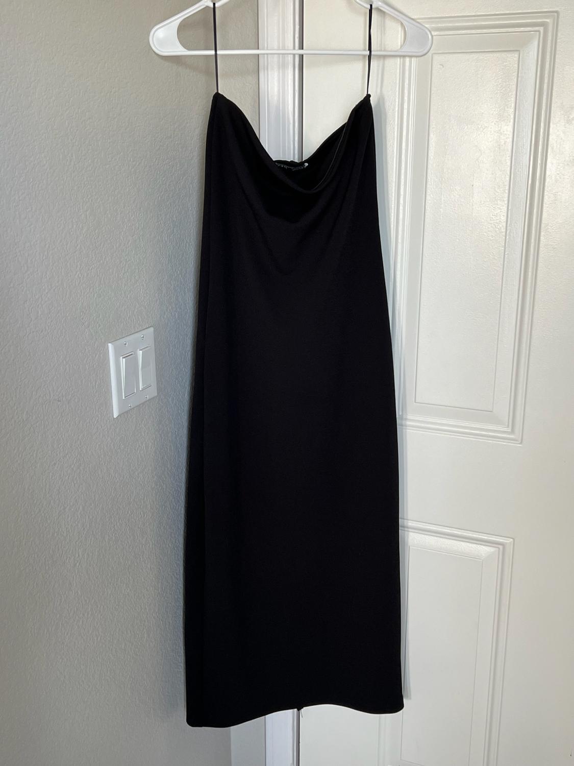 Black maxi dress with spaghetti straps and a draped neckline, hanging on a hanger over a white door in a relaxed home setting.
