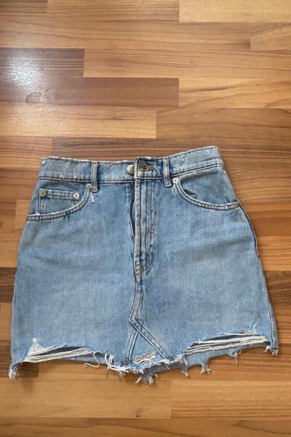 Front view of blue denim skirt with front pockets and frayed hem.