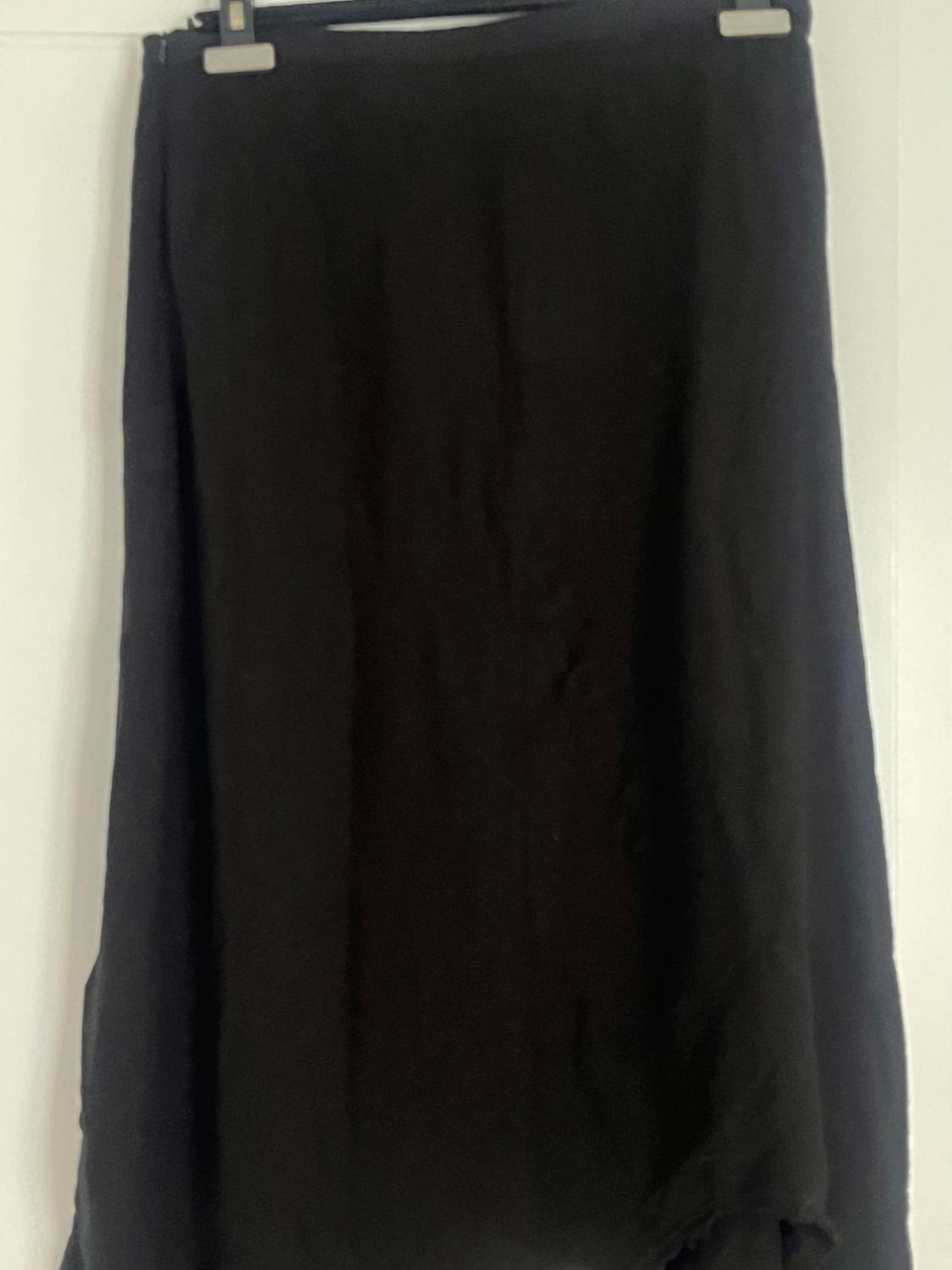 Black long skirt hanging on a hanger against a white background. The fabric appears light and flowing.