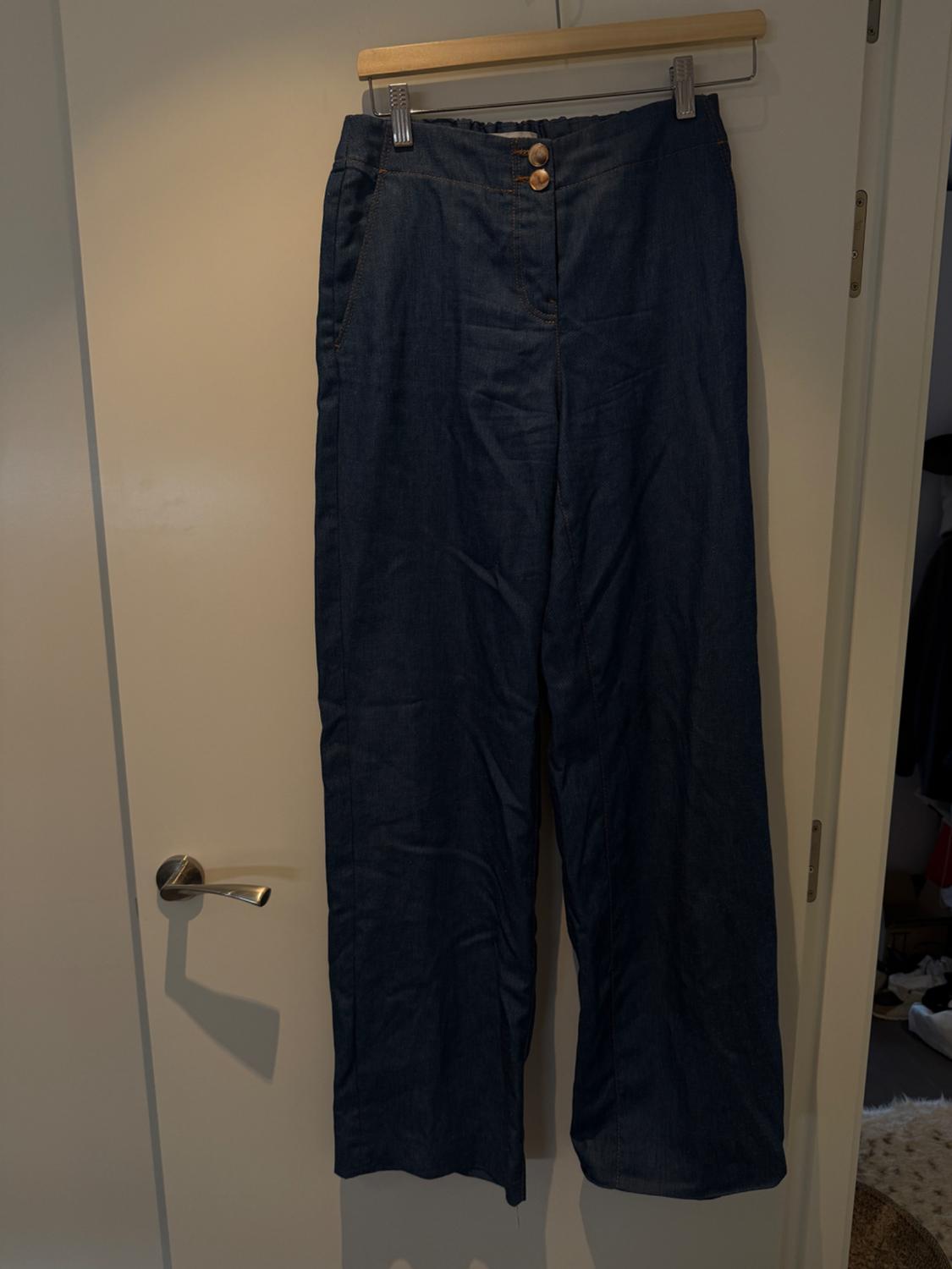 Dark blue denim trousers hanging on a wooden hanger over a white door, with two brown buttons visible.
