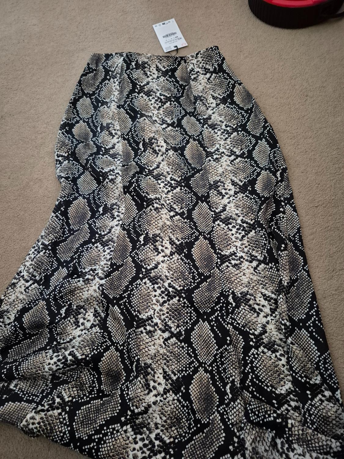 Long skirt with snake print in black and beige tones on a beige carpet. White label visible at the top.