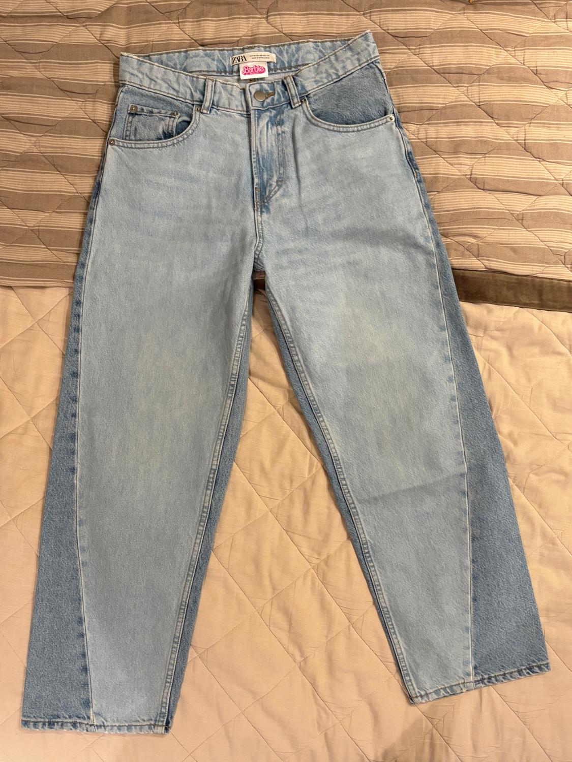 Light blue jeans with "Zara Barbie" label on the waist, on a quilted bedspread in shades of brown and beige.