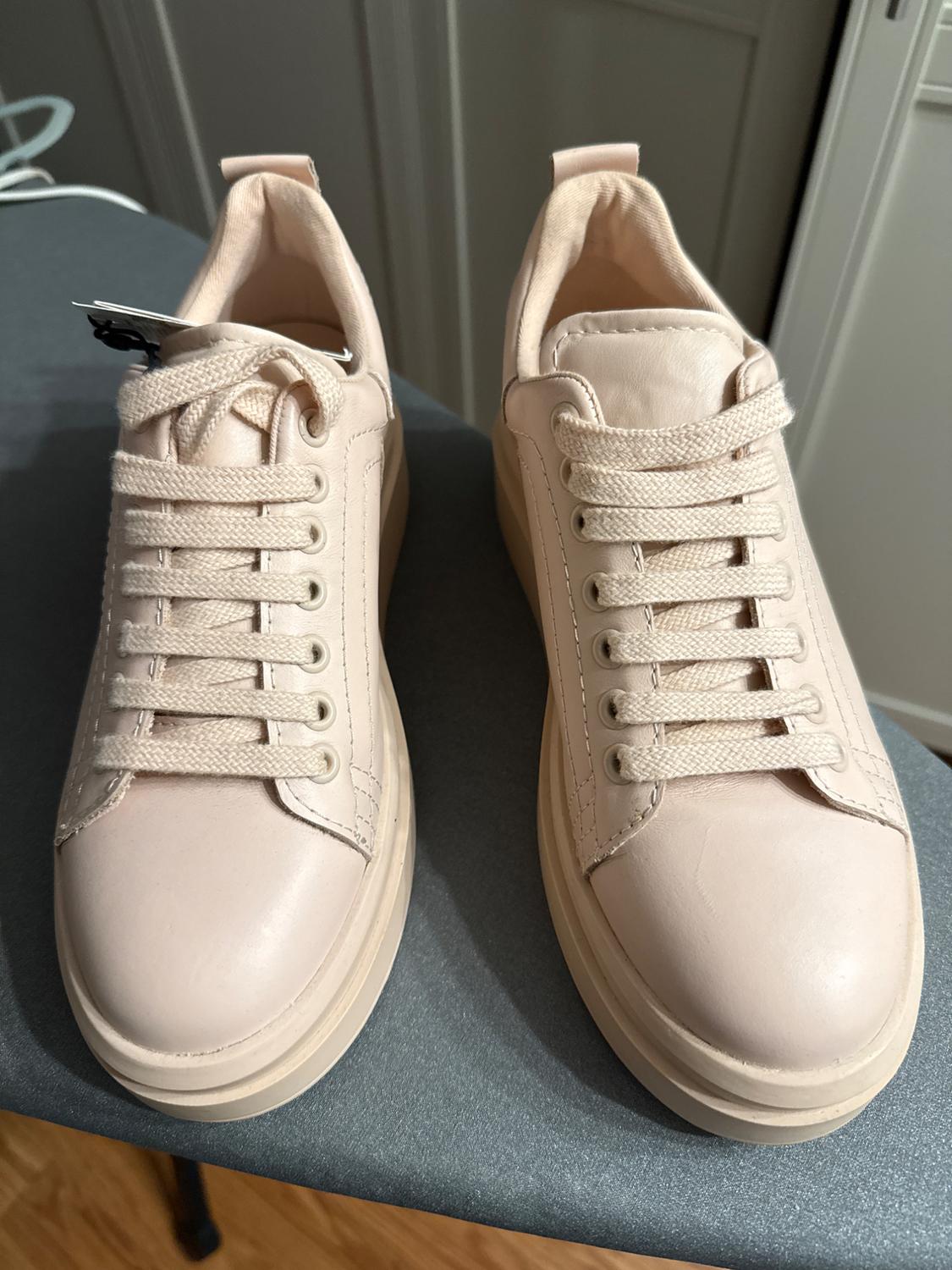 Cream-colored athletic shoes with laces on a gray surface. Background with white doors.