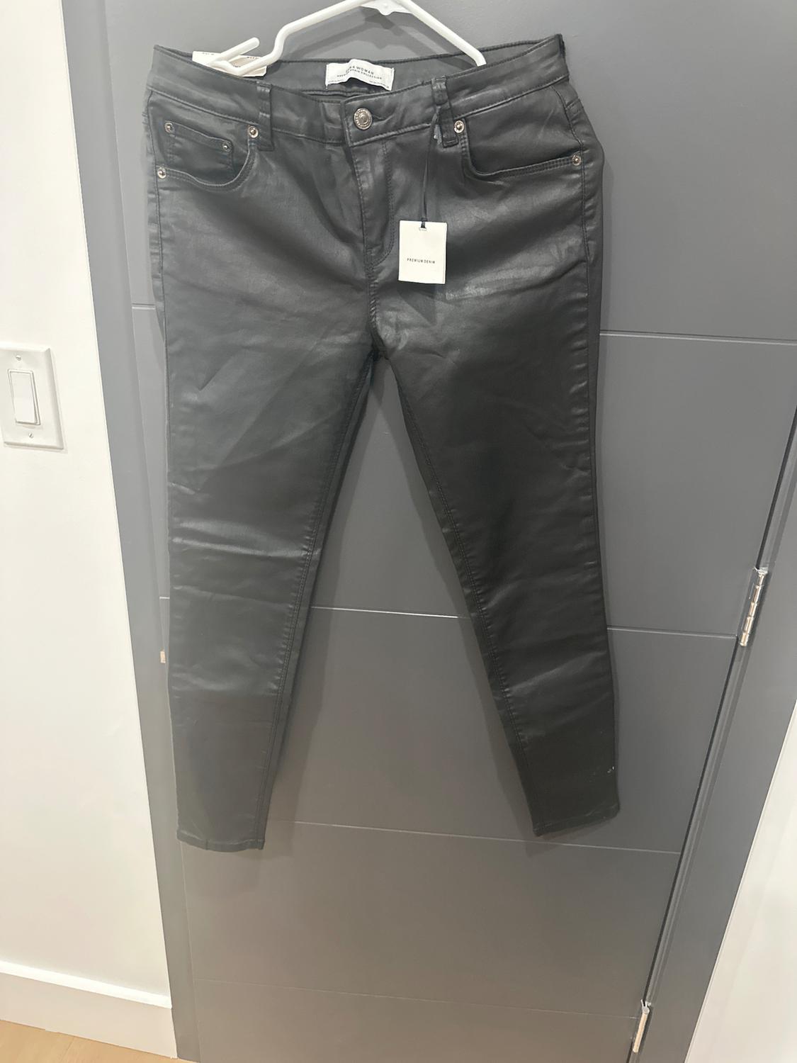 Black pants hanging on a white hanger over a gray door. Visible tag with text "PULL&BEAR".