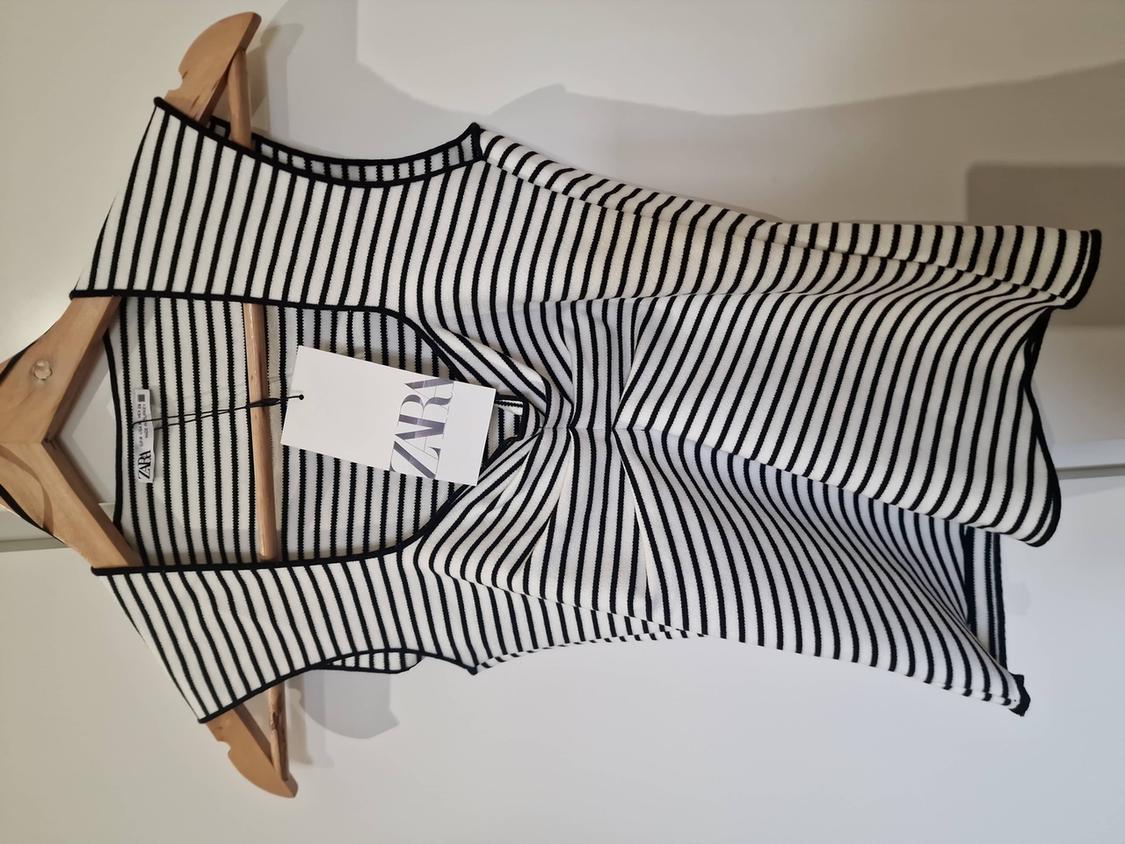 Black and white striped top hanging on a wooden hanger. Visible label with the text "ZARA". White background.