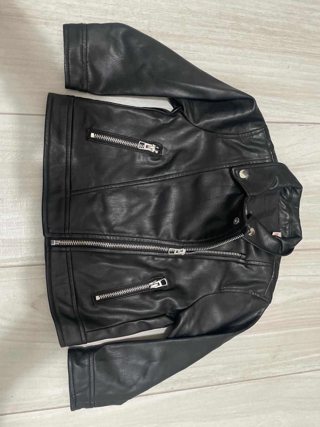 Black faux leather jacket with silver zips, on a light wooden floor.