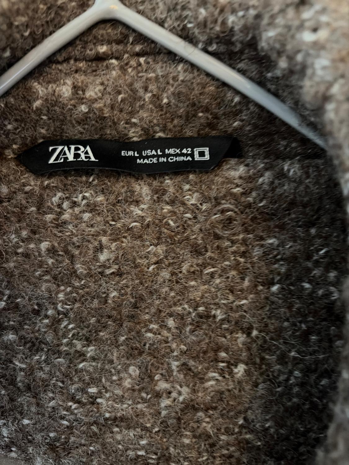 Detail of mottled brown fabric on a hanger. Black label with the text ZARA EUR L USA L MEX 42 MADE IN CHINA.