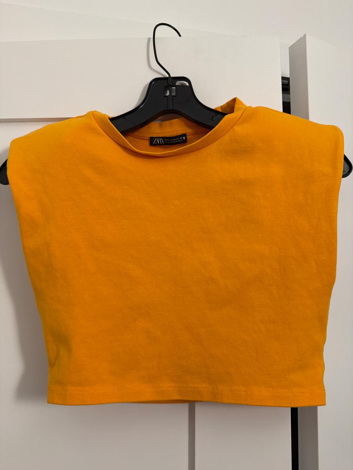 Yellow crop top hanging on a black hanger over a white door. Visible tag with text "ZARA".