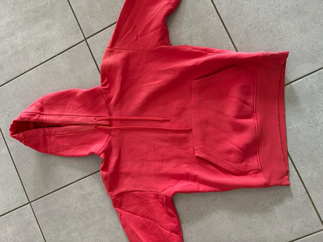 Red hooded sweatshirt with drawstring and front pocket, laid out on a grey tiled floor.