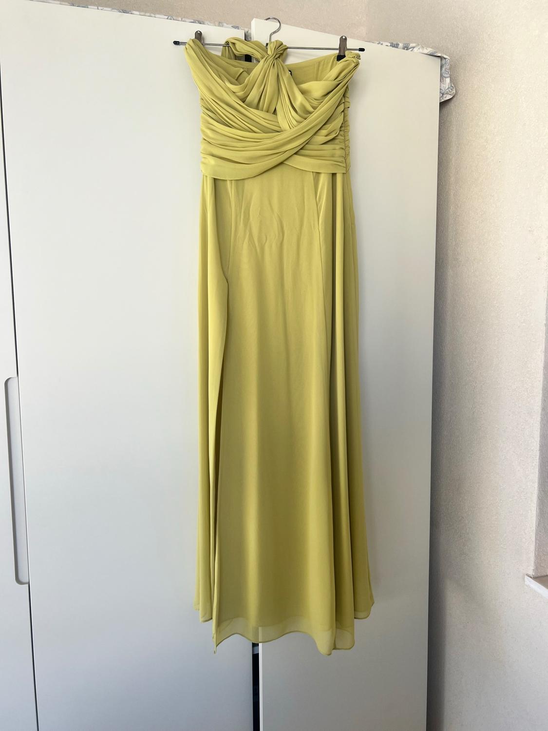 Long light-green dress with a draped neckline and flowing skirt with a slit, hanging on a hanger in a white wardrobe.