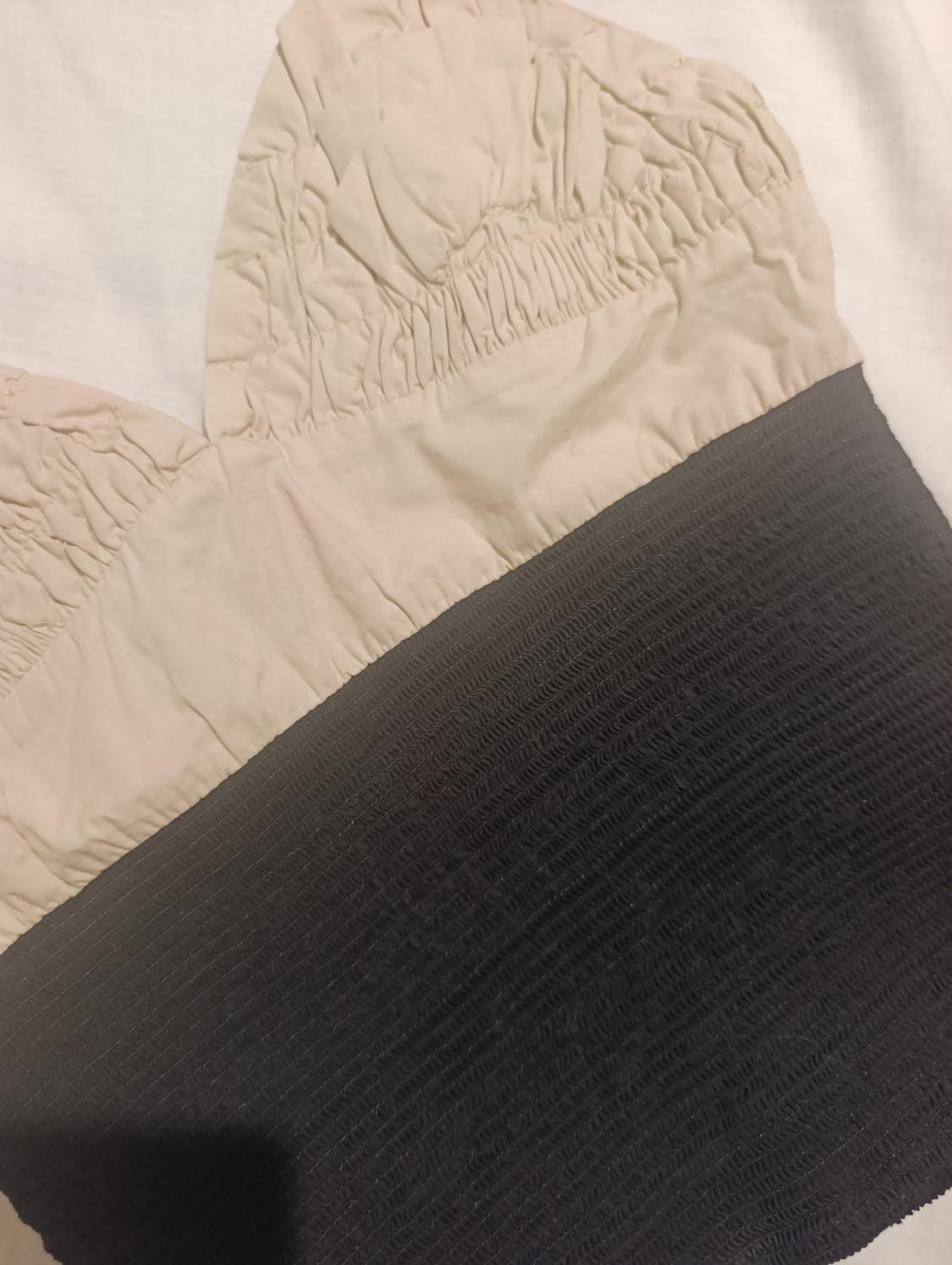 Detail of a garment with ruched texture in beige and black tones. The fabric displays a pleated and contrasting design.