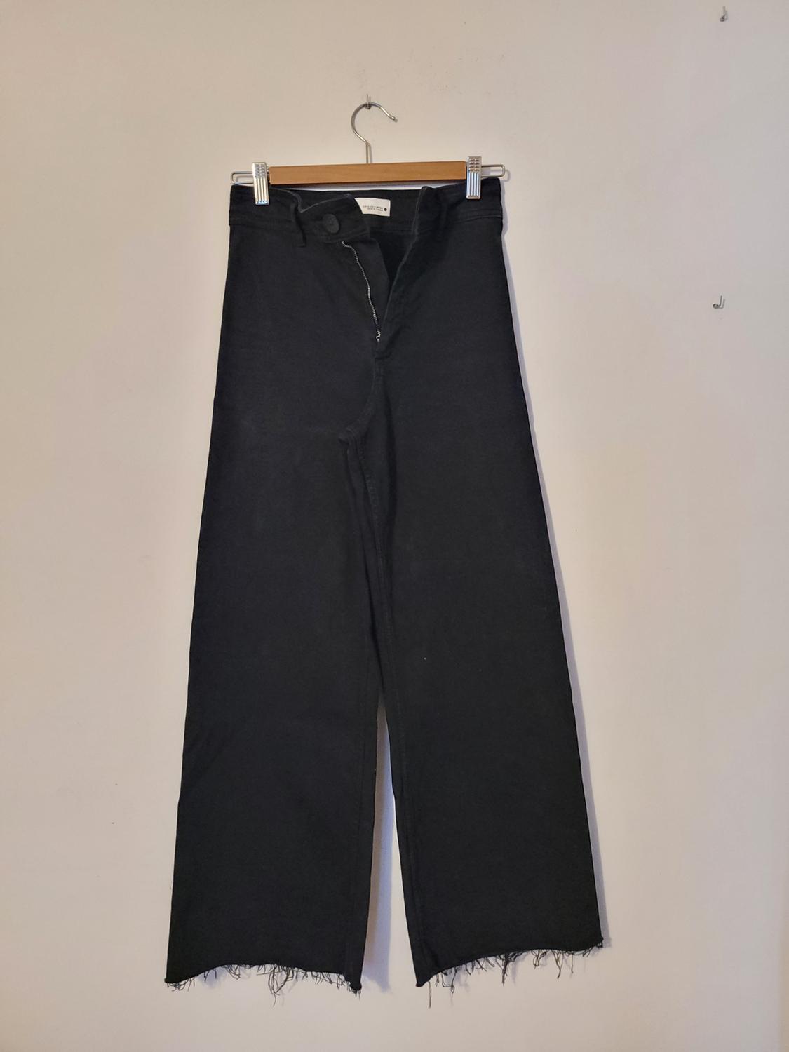 Front view of black trousers with a frayed hem and a visible zip.