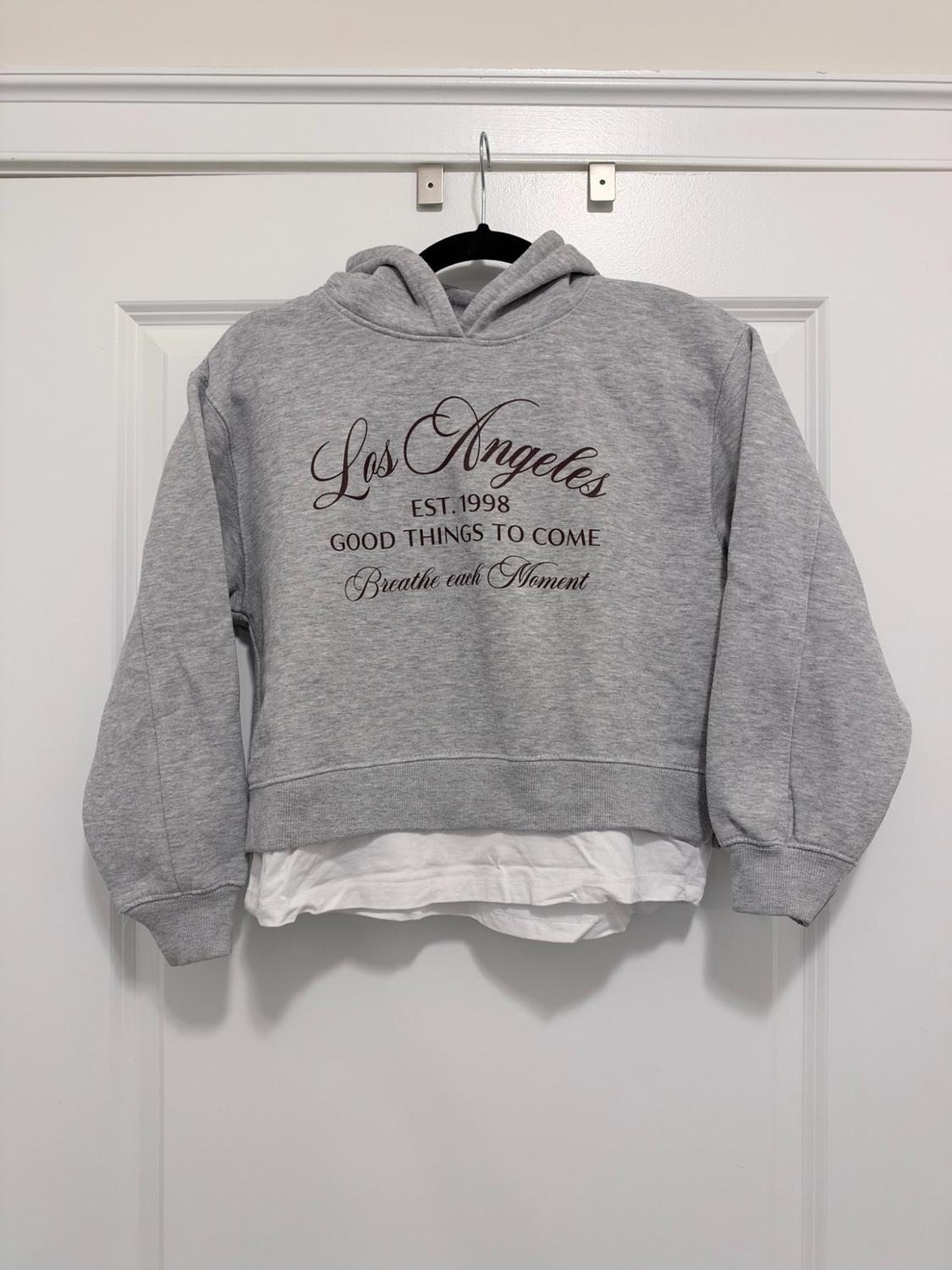Gray hooded sweatshirt hanging, white t-shirt hem underneath, and text: Los Angeles EST. 1998 GOOD THINGS TO COME Breathe each Moment.