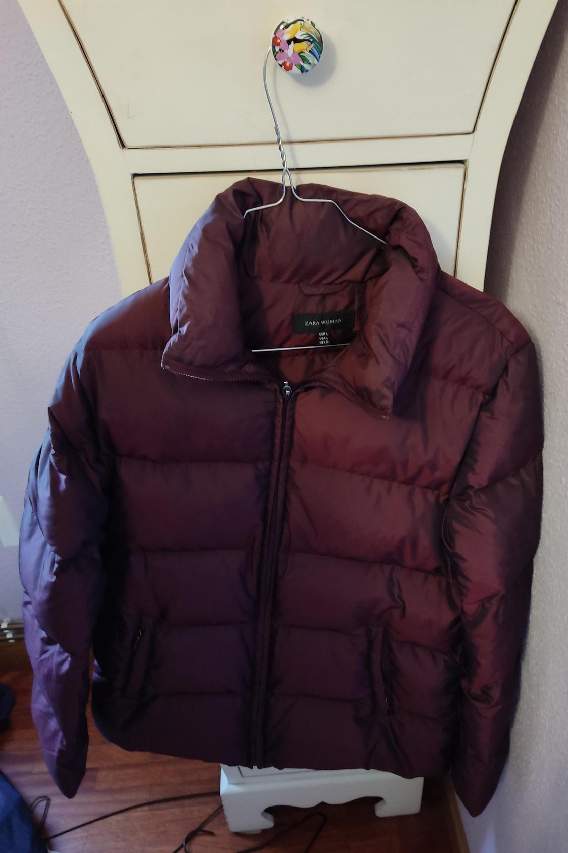 Front view of a purple quilted jacket with a zip and side pockets.