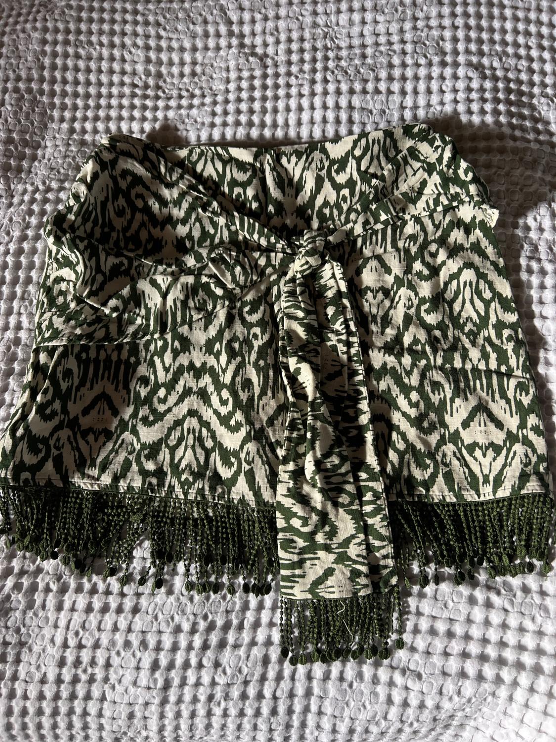 Sarong skirt with a green and white abstract print, front knot and fringed hem, on a textured white surface.