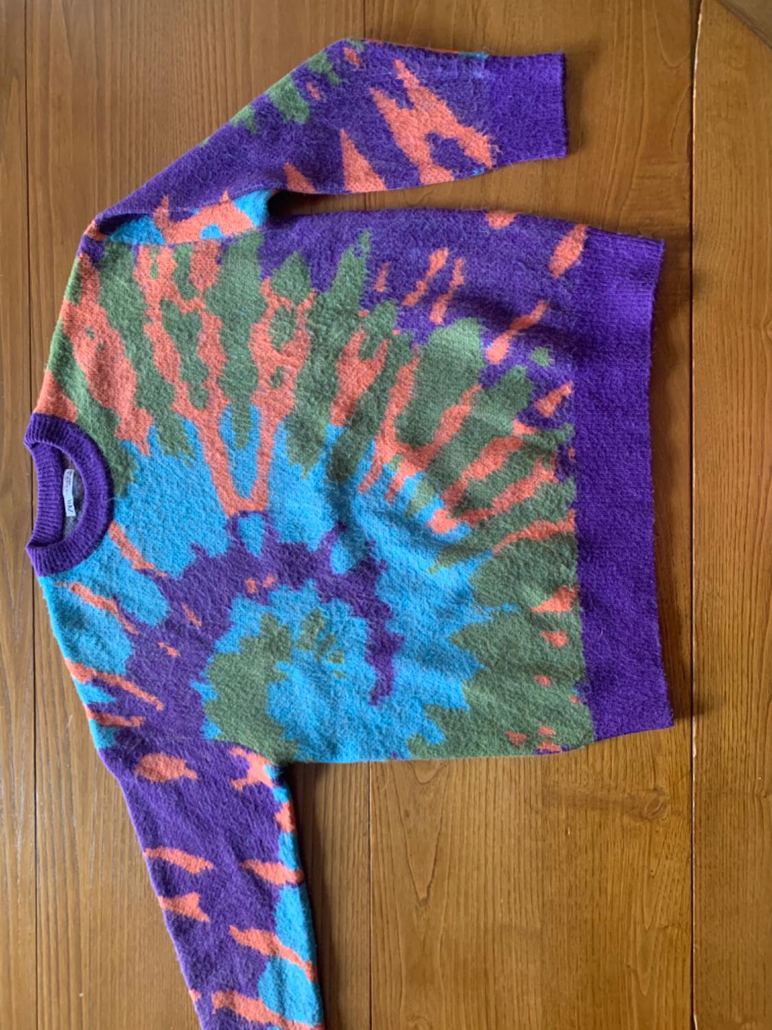 Wool jumper with a tie-dye design in shades of purple, blue, green, and orange on a wooden table.